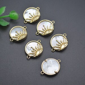 Op de afbeelding: Zes goudkleurige metalen zonnencharms met witte parelmoer inleg. Elke charm heeft een zonontwerp met een gezicht en stralen. De charms hebben twee springringen om aan sieraden te bevestigen.