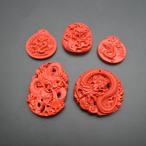 May include: Five red Chinese dragon pendants carved from cinnabar. The pendants are all different shapes and sizes, but they all feature intricate carvings of dragons.