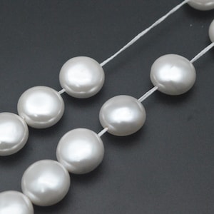 May include: Two strands of large, round, white faux pearls are strung on white thread. The pearls have a lustrous, pearlescent sheen. The background is a dark gray color. This jewelry is suitable for special occasions.
