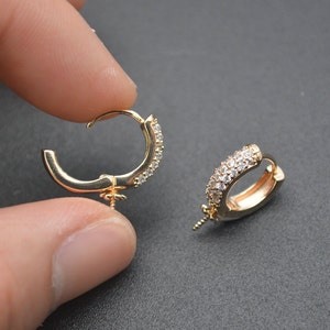 May include: Two gold hoop earrings with clear cubic zirconia stones. The earrings have a small loop at the bottom for attaching a charm.
