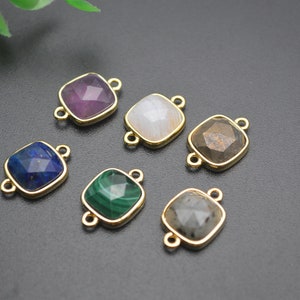 May include: A collection of square gemstone connectors in various colors, including purple, blue, green, and gray. Each stone is set in a gold-colored metal frame with two loops for attaching to other components. The gemstones are faceted, and the background is black.