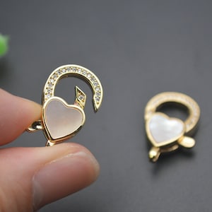 May include: Two gold-tone heart-shaped clasps with clear crystal accents. The clasps are designed to be used as a connector for jewelry.