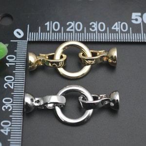 May include: Two metal jewellery clasps. One is gold-toned, the other is silver-toned. Each clasp has a round ring and a barrel-shaped end. The clasps are approximately 1.3 cm in diameter.
