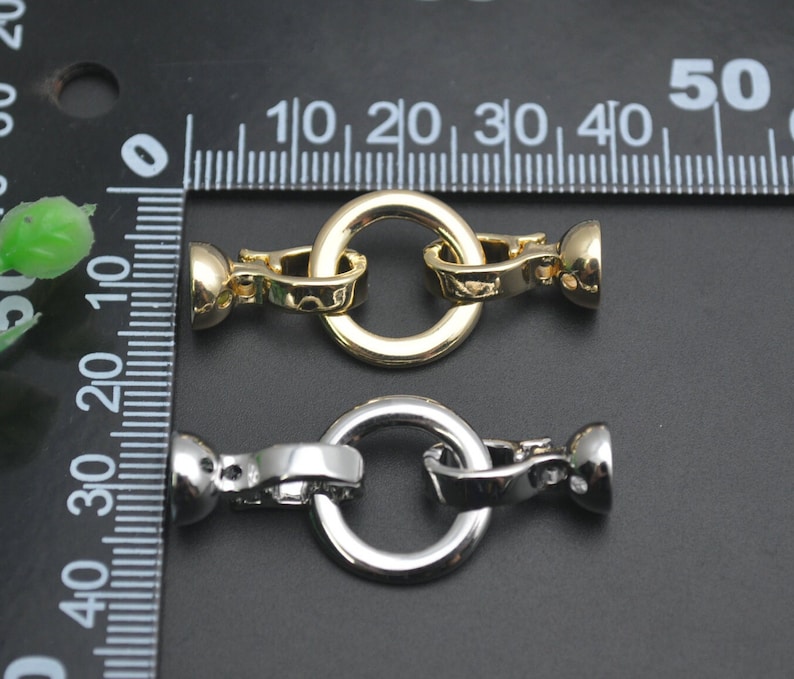 May include: Two metal jewellery clasps. One is gold-toned, the other is silver-toned. Each clasp has a round ring and a barrel-shaped end. The clasps are approximately 1.3 cm in diameter.