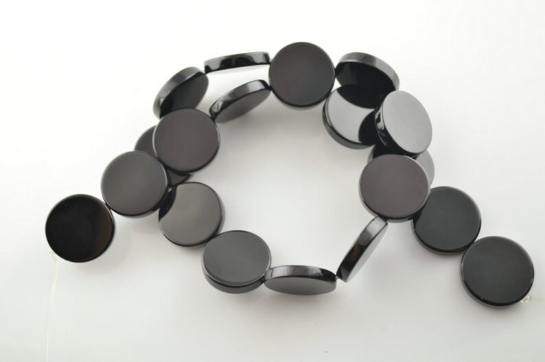 May include: A strand of black round gemstone beads. The beads are smooth and polished, and they are strung on a white thread.
