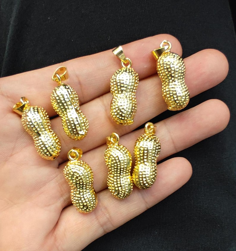 May include: Eight gold peanut-shaped pendants with a textured surface. The pendants are arranged on a hand.