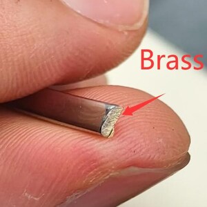 May include: Close-up of a brass metal strip with a textured, angled edge. The word "Brass" is written in red. The metal strip is held between fingers.