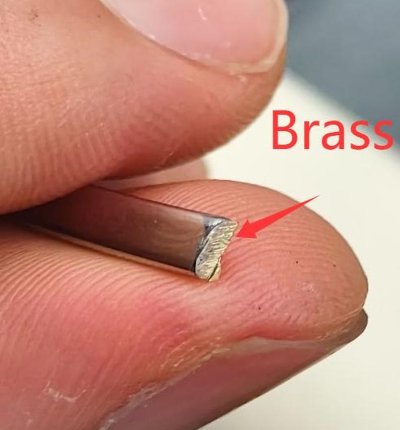 May include: Close-up of a brass metal strip with a textured, angled edge. The word "Brass" is written in red. The metal strip is held between fingers.