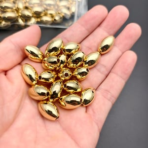 Peut inclure: Un ensemble de perles ovales brillantes de couleur dorée. Les perles ont une surface lisse et réfléchissante et sont regroupées. Certaines perles sont nettes, tandis que d'autres sont légèrement floues. Les perles mesurent environ 1,3 cm de long.