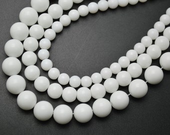 Peut inclure: Un collier de perles rondes blanches, de différentes tailles, disposées en cercle sur une surface noire.