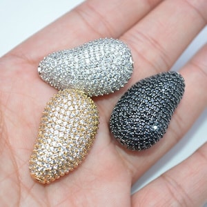 May include: Three teardrop-shaped beads with a pave setting of clear and black cubic zirconia stones. The beads are approximately 1 inch long.