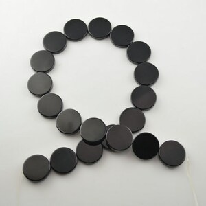 May include: A strand of black round beads, strung on a white cord. The beads are all the same size and shape, and they are arranged in a circle.