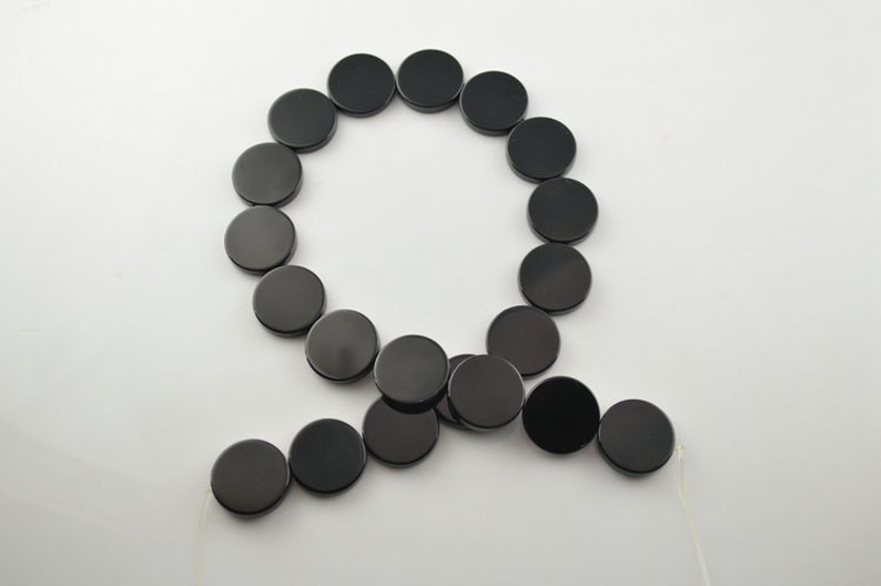 May include: A strand of black round beads, strung on a white cord. The beads are all the same size and shape, and they are arranged in a circle.