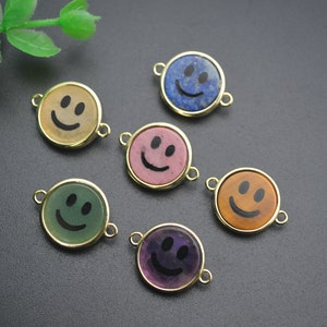 May include: Six gold-toned charms with different colored stone inlays, each featuring a black smiley face design.