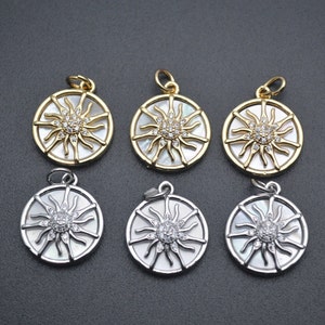 Puede incluir: Seis colgantes de sol de oro y plata con detalles de nácar blanco y cristal transparente. Los colgantes son redondos y tienen un diseño de sol con rayos que emanan del centro.