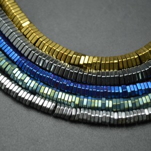 May include: A collection of faceted gemstone beads in various colors, including gold, silver, blue, and black. The beads are arranged in a semi-circle, showcasing their unique shape and shine.
