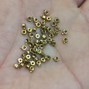 May include: A pile of small, gold-coloured metal rings with a small loop on one side. The rings are scattered on a hand.