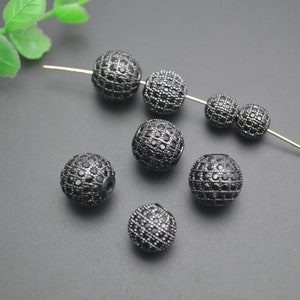 May include: Black round beads with small black rhinestones covering the surface. The beads are scattered on a gray surface.
