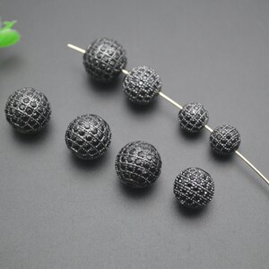 May include: Black round beads with a diamond-like pattern. The beads are strung on a thin wire.
