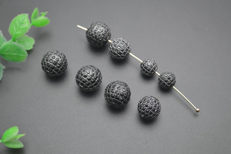 May include: Black round beads with a diamond-like pattern. The beads are strung on a thin wire.
