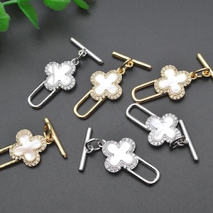 May include: Five silver and gold tone metal toggle clasps with a white clover design. Each clasp has a T-bar and a loop.