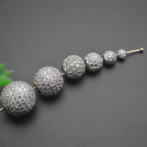 May include: A set of six silver-toned round beads, each covered in small, clear rhinestones. The beads are arranged in a line, decreasing in size from left to right.