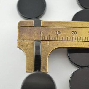 May include: A brass caliper measuring the diameter of a black round object. The caliper has a scale marked in millimetres from 0 to 40.