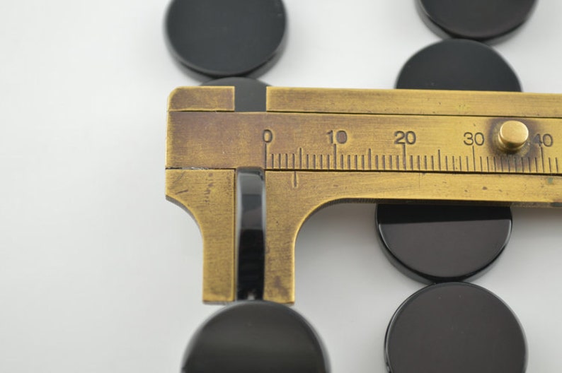 May include: A brass caliper measuring the diameter of a black round object. The caliper has a scale marked in millimetres from 0 to 40.