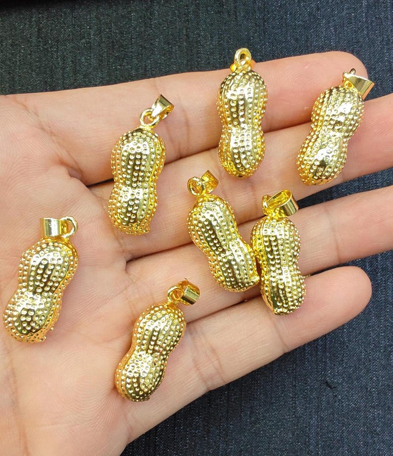 May include: Six gold-colored peanut-shaped pendants with a textured surface. The pendants are on a hand.