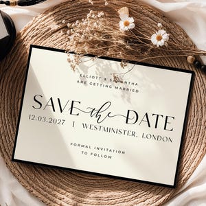 May include: A cream-coloured wedding 'Save the Date' card with black text and border. The card includes the names of the couple, the date 12.03.2027, and the location, Westminster, London. The card is displayed on a woven mat with floral and bead decorations.