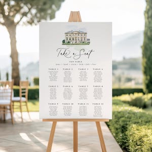 Op de afbeelding: Een witte trouwzittingstafel op een houten ezel. De kaart toont een aquarel illustratie van een gebouw, met de woorden "Take a Seat" in elegant schrift. Namen staan onder de tafelnummers.