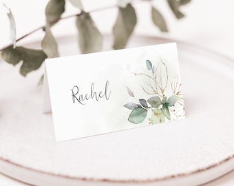 May include: A white place card with a green and gold watercolor floral design. The name "Rachel" is written in black cursive script.