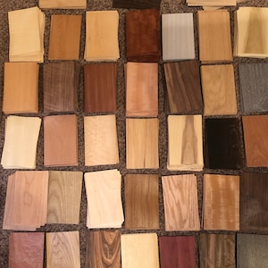Könnte beinhalten: Eine Sammlung von Holzfurnierproben in verschiedenen Farben und Mustern, darunter hellbraun, dunkelbraun, rot und grau. Die Proben sind in einem Rastermuster auf einer braunen Oberfläche angeordnet.