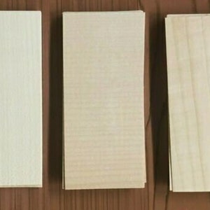 May include: Three wooden boards, each with a different wood grain pattern. The board on the left has a light, almost white, grain. The middle board has a light brown grain. The board on the right has a medium brown grain.