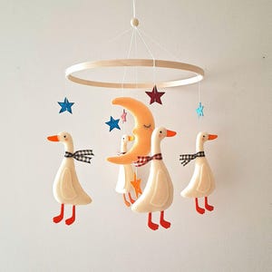 Pode incluir: Móvel de berço com gansos de feltro, bicos e pés laranja, e laços xadrez. Uma lua crescente e estrelas penduradas em um anel de madeira. Uma decoração encantadora para o quarto do bebê.
