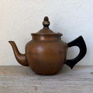 May include: A vintage copper teapot with a wooden knob on the lid and a black plastic handle.