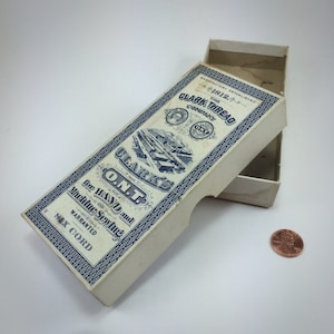 May include: A vintage box of Clark's O.N.T. Six Cord thread for hand and machine sewing. The box is white with blue lettering and a design of a factory. The text on the box reads "Clark's O.N.T. for Hand and Machine Sewing. Warranted Six Cord."