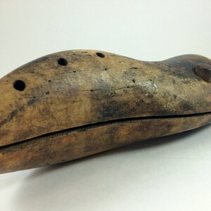 May include: A wooden shoe stretcher with a metal handle. The stretcher is brown and has a few holes in it. It is used to help stretch shoes to fit better.