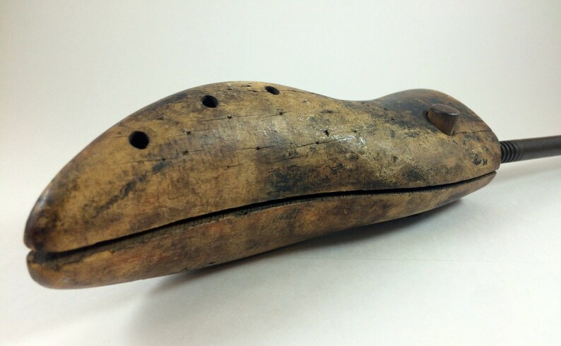 May include: A wooden shoe stretcher with a metal handle. The stretcher is brown and has a few holes in it. It is used to help stretch shoes to fit better.