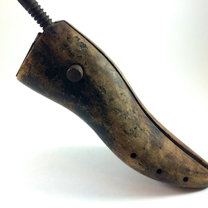 May include: A vintage wooden shoe stretcher with a metal screw and a knob. The stretcher is brown and has a worn finish.