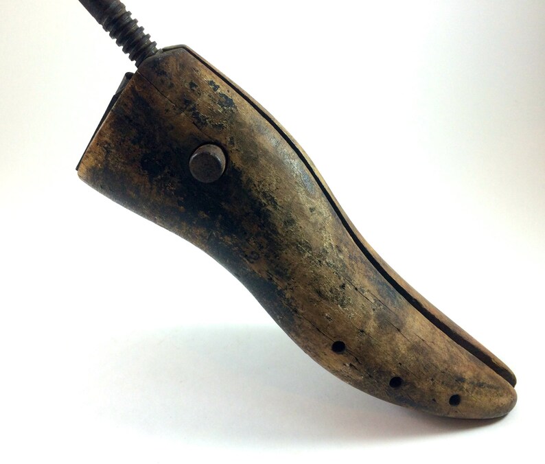 May include: A vintage wooden shoe stretcher with a metal screw and a knob. The stretcher is brown and has a worn finish.