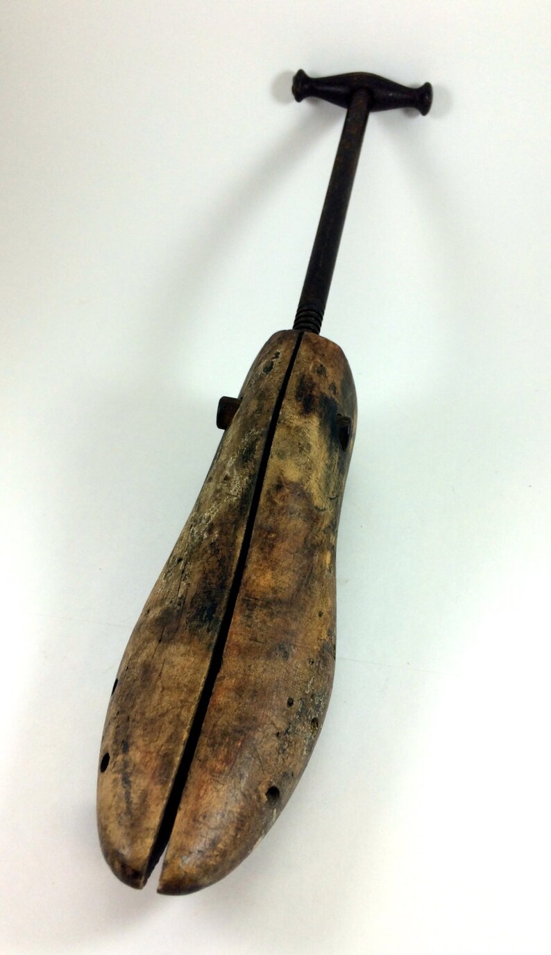 May include: A wooden shoe stretcher with a metal handle. The stretcher is made of two pieces of wood that are joined together by a metal screw. The handle is attached to the screw and can be turned to adjust the width of the stretcher.