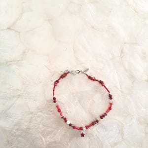 May include: A red beaded anklet with a silver clasp and a small red gemstone charm.