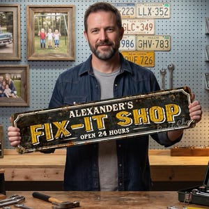 Könnte beinhalten: Ein rechteckiges Metallschild mit abgenutzter schwarzer Oberfläche und gelber Aufschrift Alexander's FIX-IT SHOP OPEN 24 HOURS. Das Schild hat einen dekorativen Rand und ein verwittertes, an Vintage-Objekte erinnerndes Aussehen.