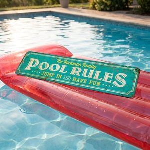 May include: A rectangular teal metal sign with rounded corners and a distressed finish. The text reads: The Ruckman Family POOL RULES JUMP IN AND HAVE FUN. The sign features small holes at each corner for mounting and white lettering.