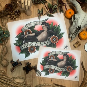 May include: Two prints of a tattoo design featuring a man with the text "Life... um... finds a way." The design is in a traditional tattoo style with red, green, and brown colors.