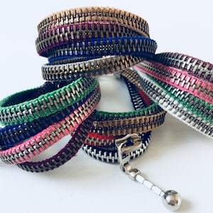 May include: A set of colourful zipper bracelets with different coloured threads and metal zipper teeth. The bracelets are stacked on top of each other.
