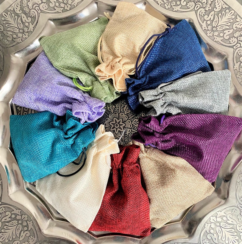 K&ouml;nnte beinhalten: Eine Sammlung von 10 kleinen, mit Kordel zu schlie&szlig;enden Beuteln aus verschiedenen Stoffen, darunter Jute, Leinen und Baumwolle. Die Beutel sind in einem Kreis auf einem silbernen Tablett angeordnet. Die Beutel sind in verschiedenen Farben, darunter Lila, Blau, Gr&uuml;n, Rot und Beige.