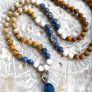 K&ouml;nnte beinhalten: Eine blaue, wei&szlig;e und braune Mala-Halskette mit einem blauen Quasten und Abalone-Muschel-Akzenten.