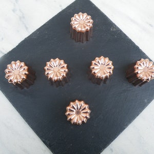 Può includere: Sei stampi rotondi per torte in rame, scanalati, con un motivo floreale decorativo su una superficie in ardesia nera.